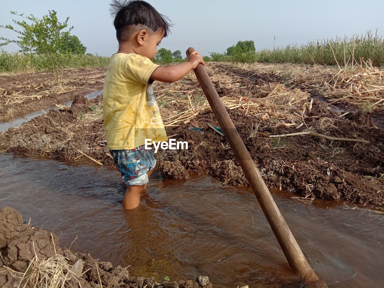 FULL LENGTH OF BOY STANDING IN MUD ON DIRT ROAD