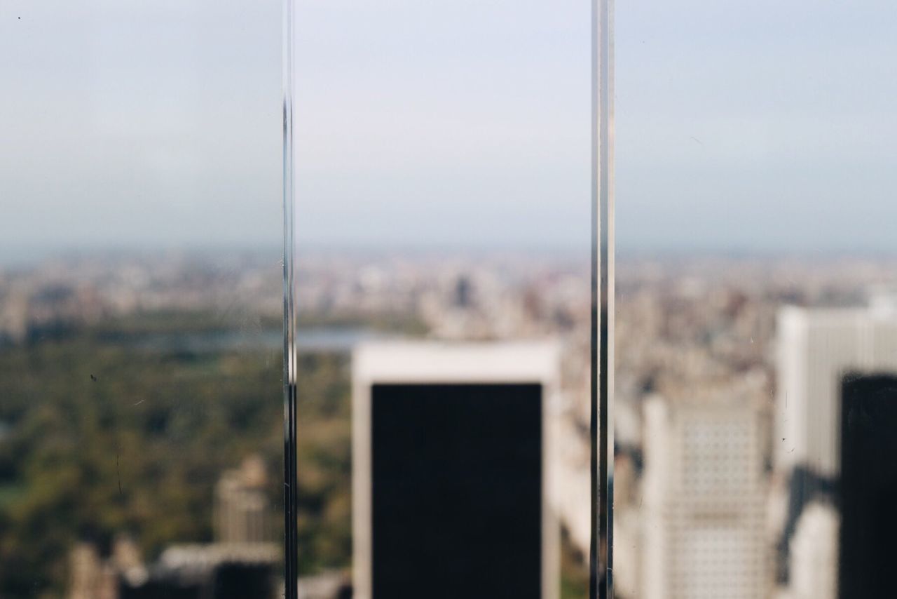 Close-up of glass window by cityscape against sky