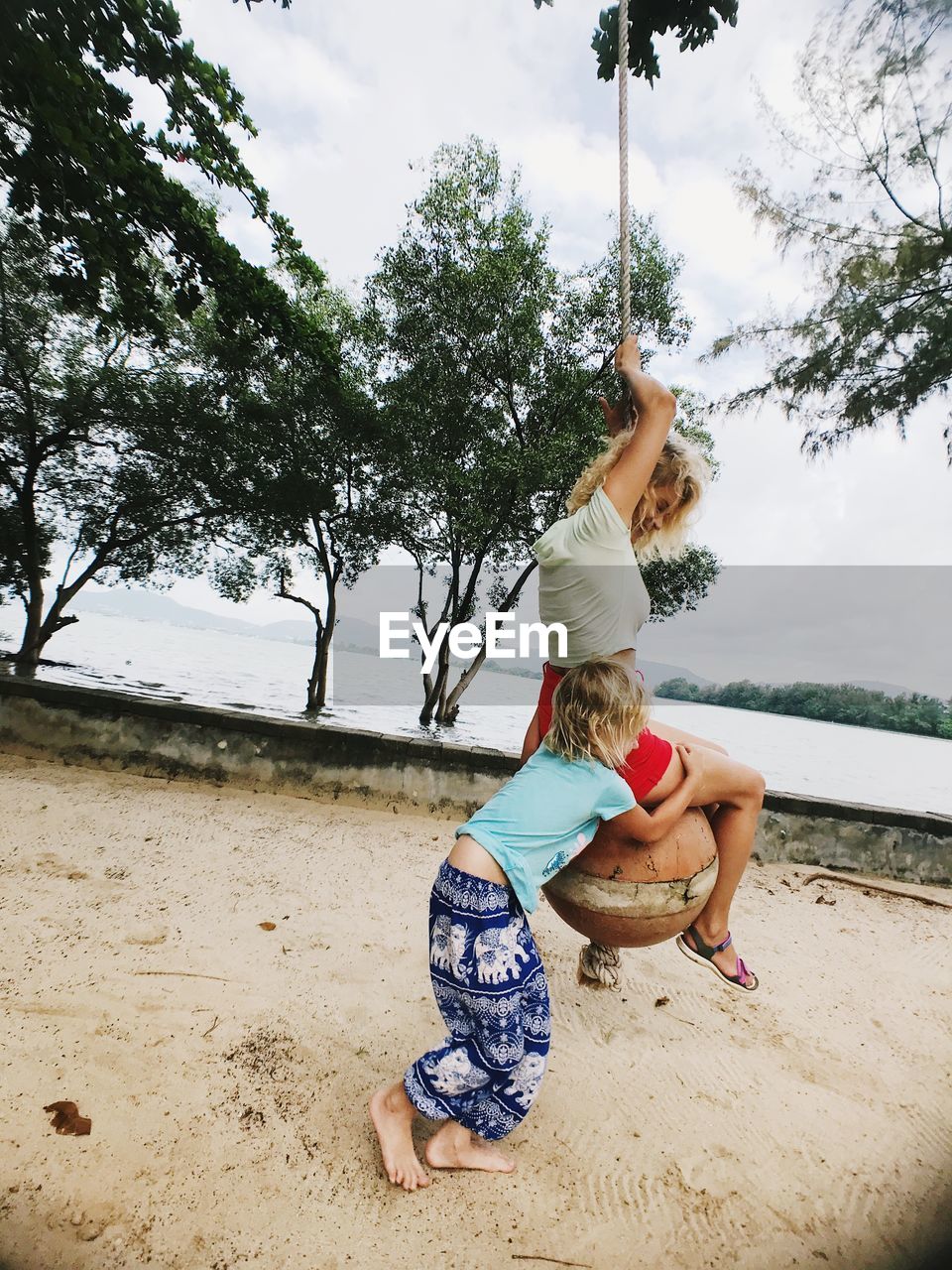 Girl embracing woman sitting on rope swing 