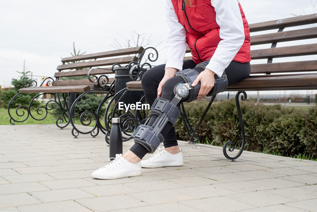 Woman wearing sport clothes and knee brace or orthosis after leg surgery, walking in the park