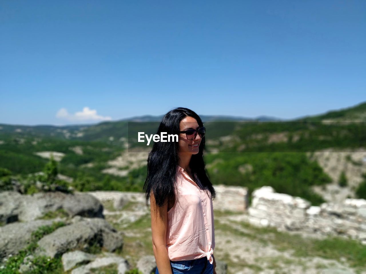 Portrait of young woman wearing sunglasses standing on mountain against sky