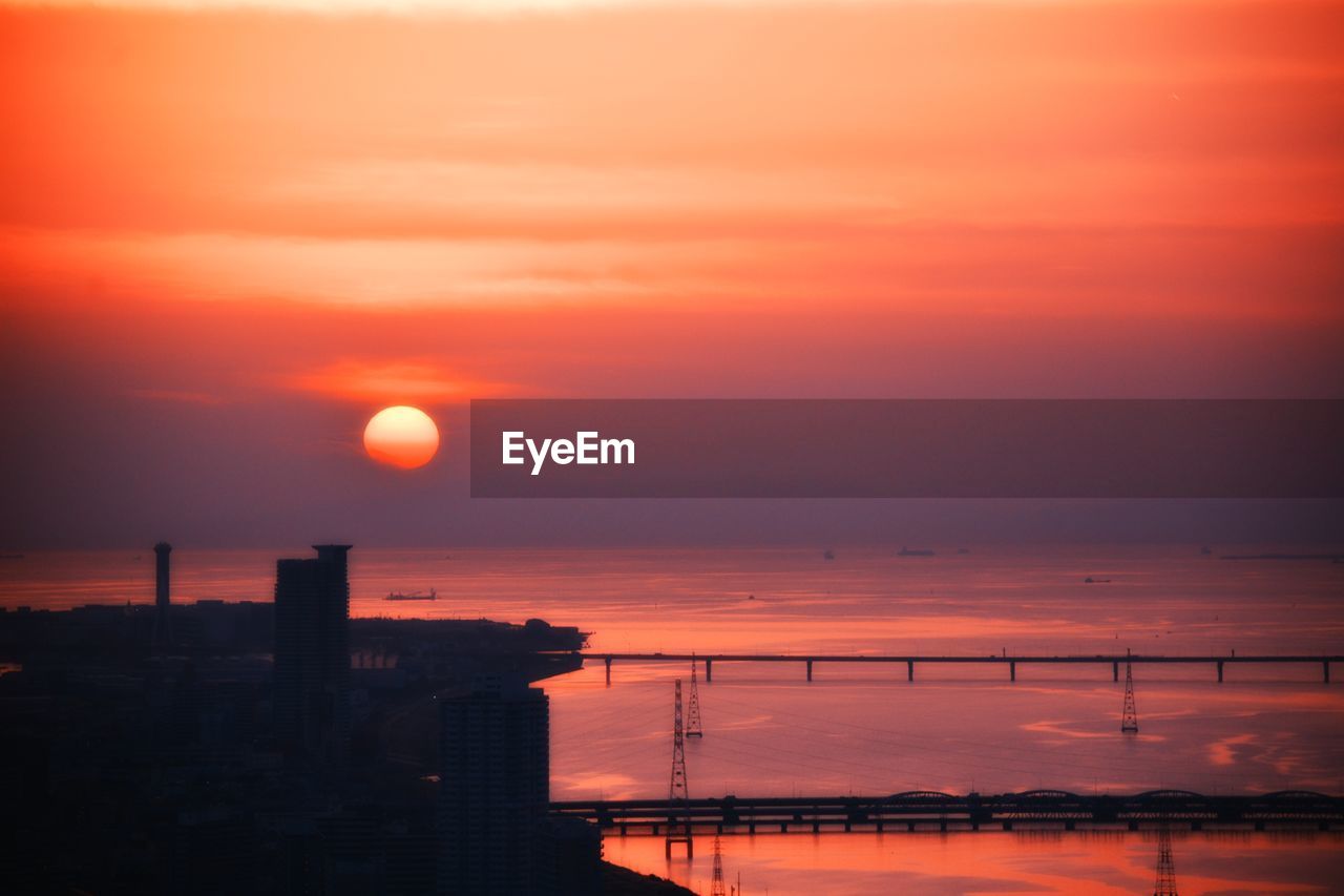 Cityscape by sea against sky during sunset