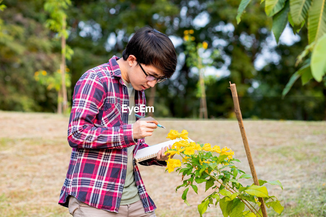 Man writing in book while standing by plant