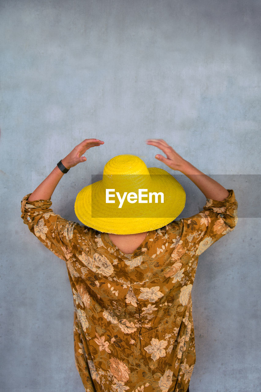 Rear view of young woman wearing yellow sun hat by wall