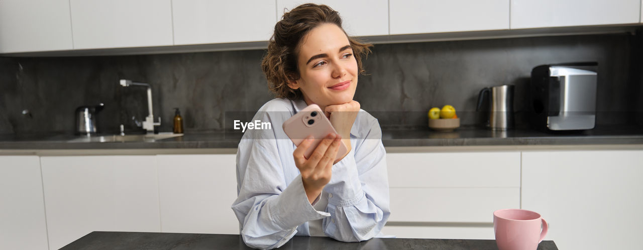 portrait of young woman using phone while sitting on table at home