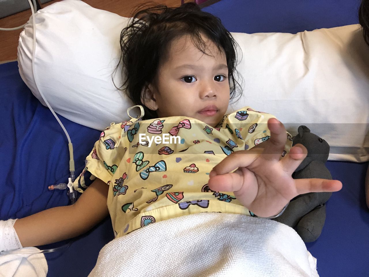 High angle portrait of girl gesturing while lying on bed in hospital