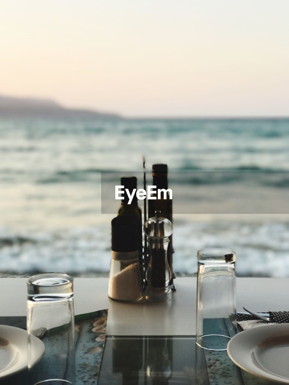 Tableware on table by sea against sky during sunset