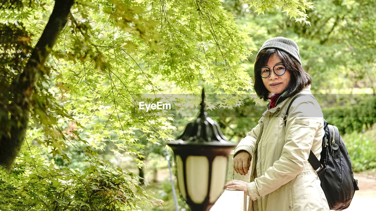 Portrait of young woman standing against trees