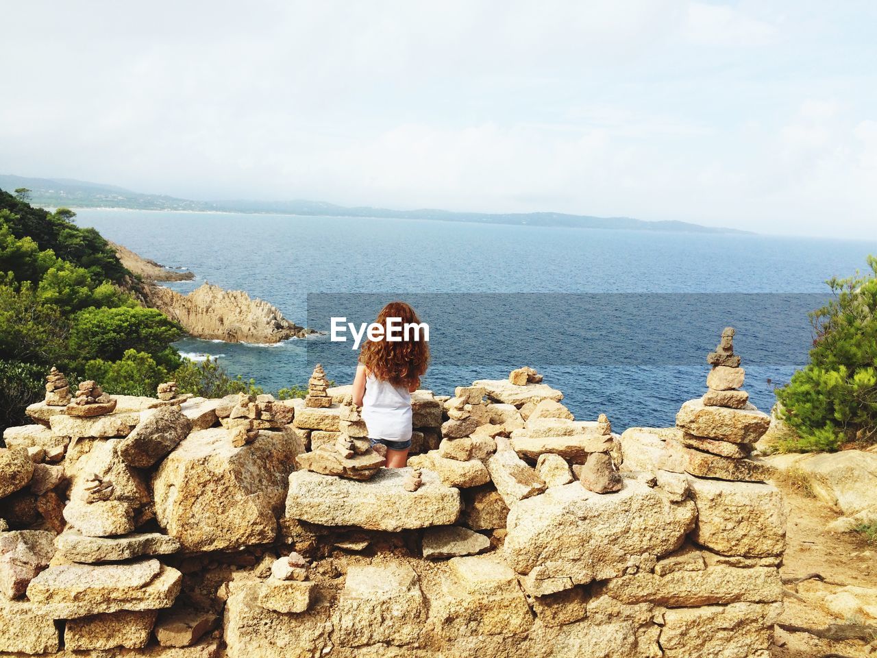 Rear view of girl standing amidst stone stacks looking at sea