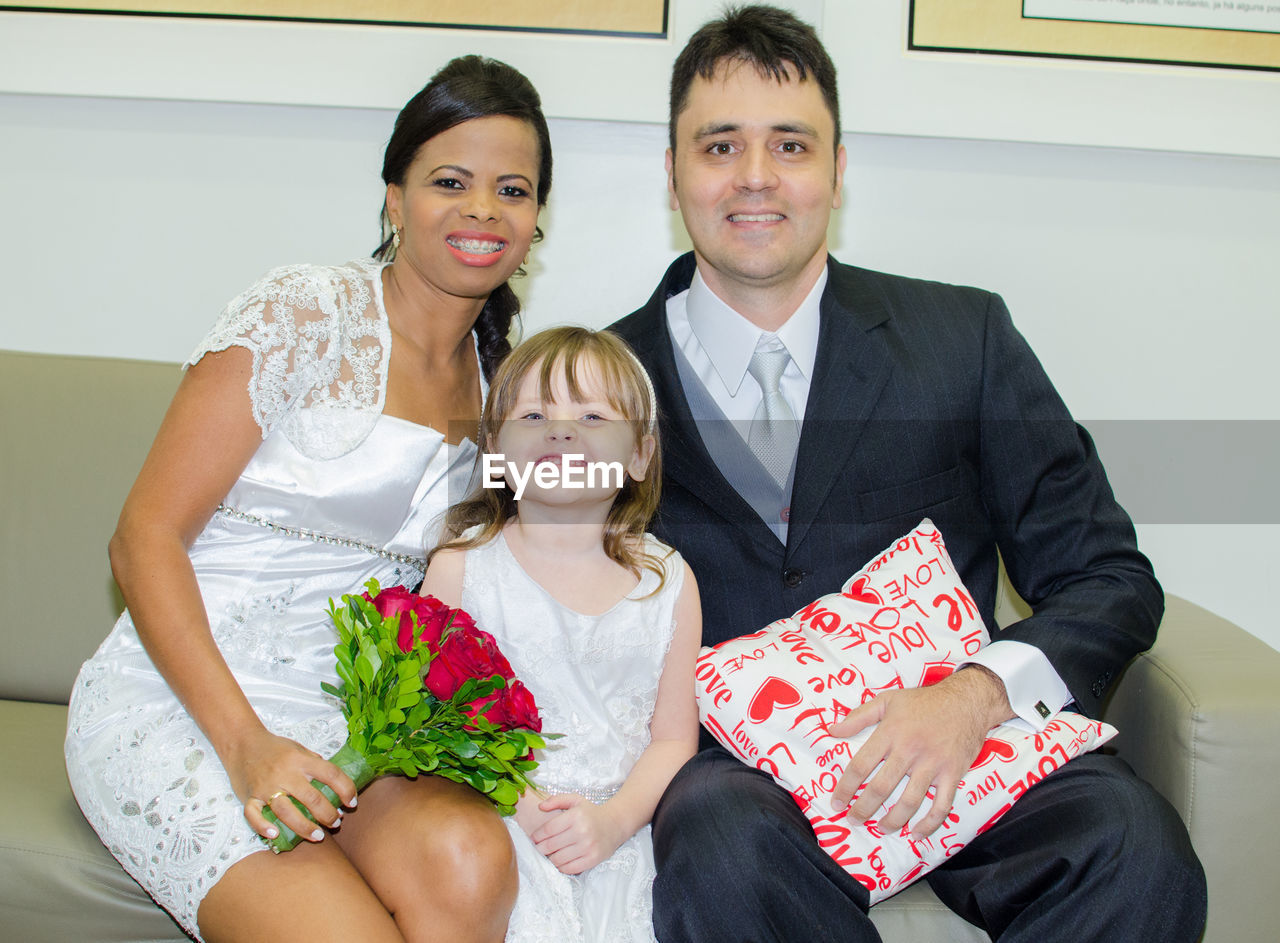 Portrait of smiling young couple sitting with daughter on sofa at home