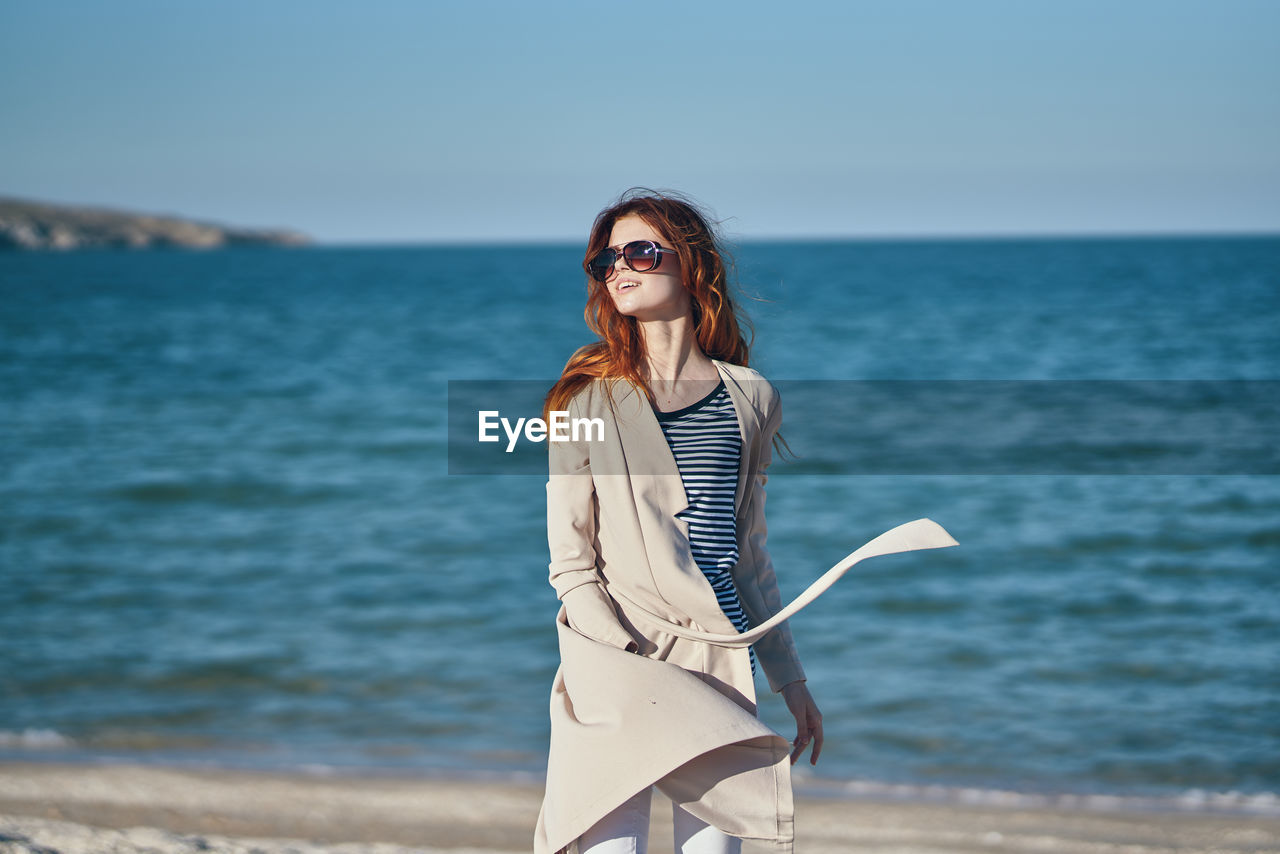 Young woman standing at beach against sky