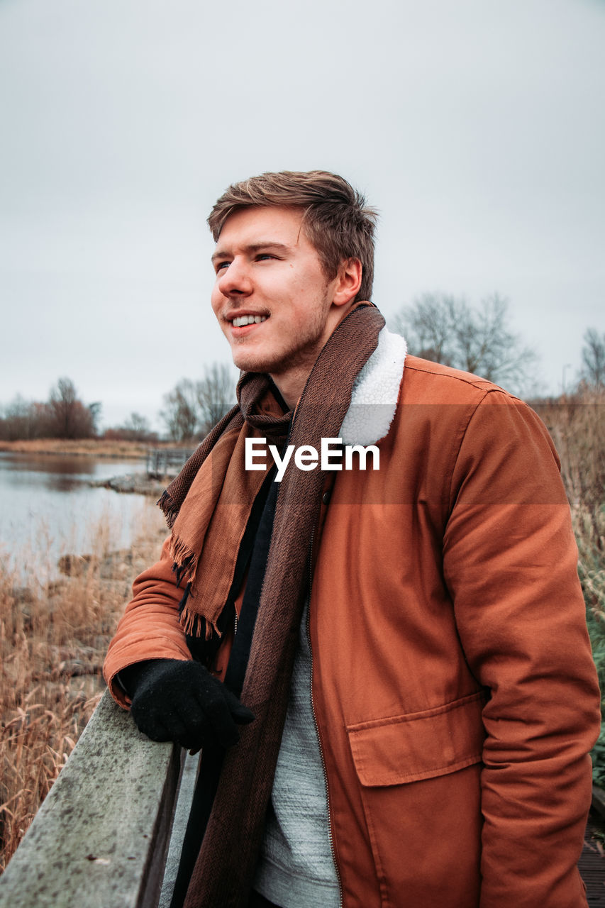 Young man looking away while standing by railing