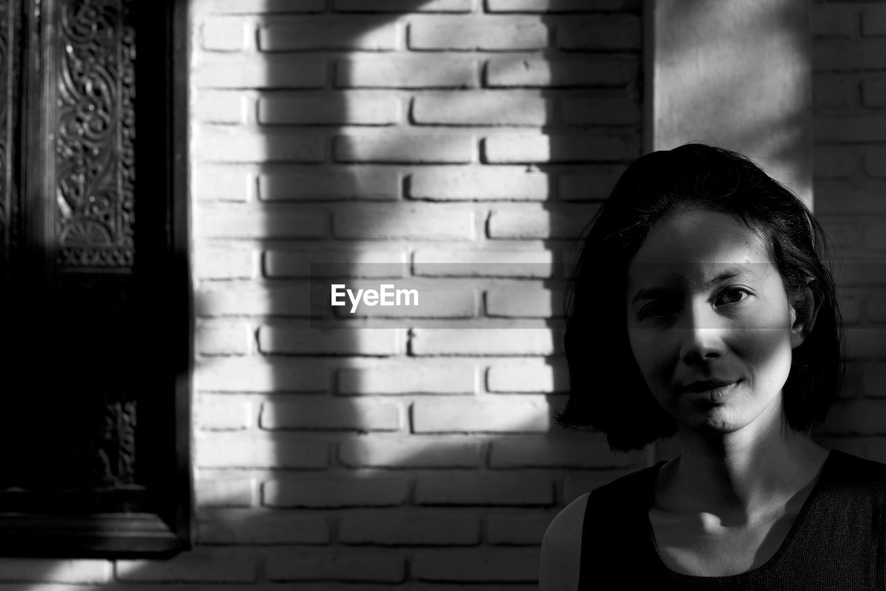 Portrait of young woman against brick wall at home