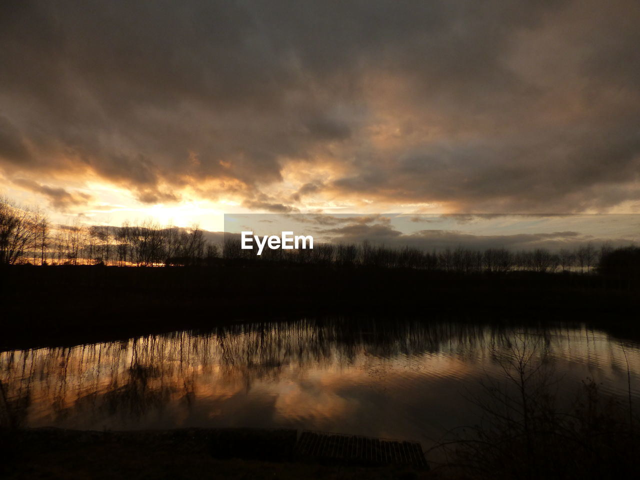 REFLECTION OF SILHOUETTE TREES ON LAKE AGAINST SKY