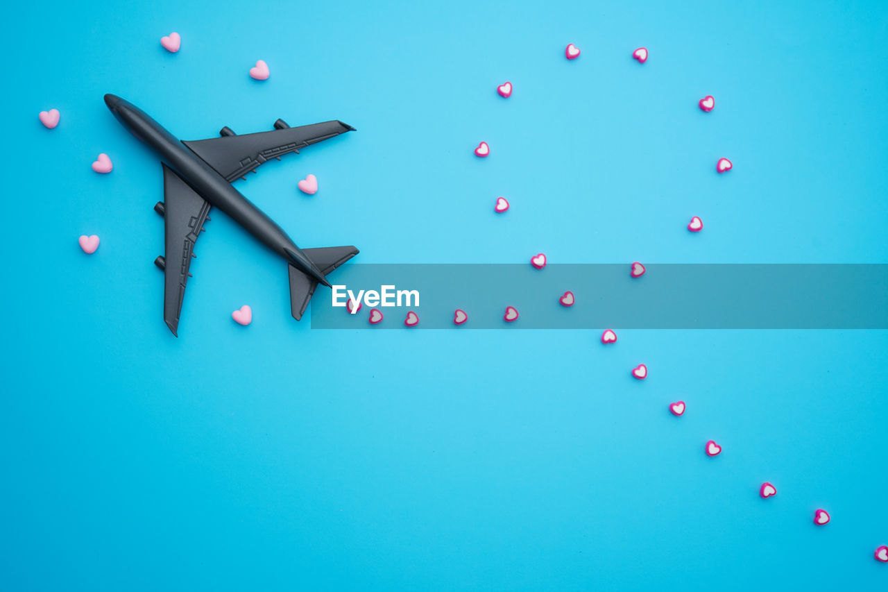 Travel valentine day concept flat lay design with airplane and heart shape beads on blue background 