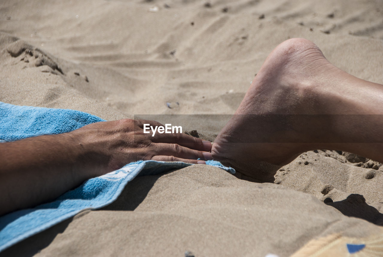 Low section of man relaxing on sand at beach