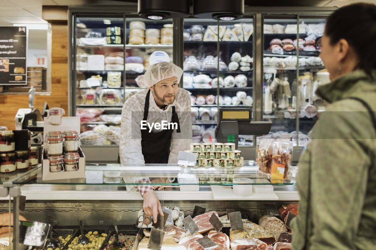 Sales clerk looking at female customer while assisting at supermarket