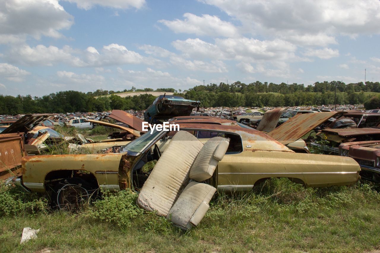 Old abandoned cars on grassy field against sky
