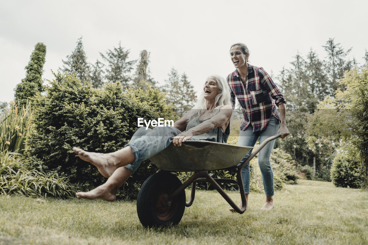 Daughter pushing mother, sitting in push cart, through the garden