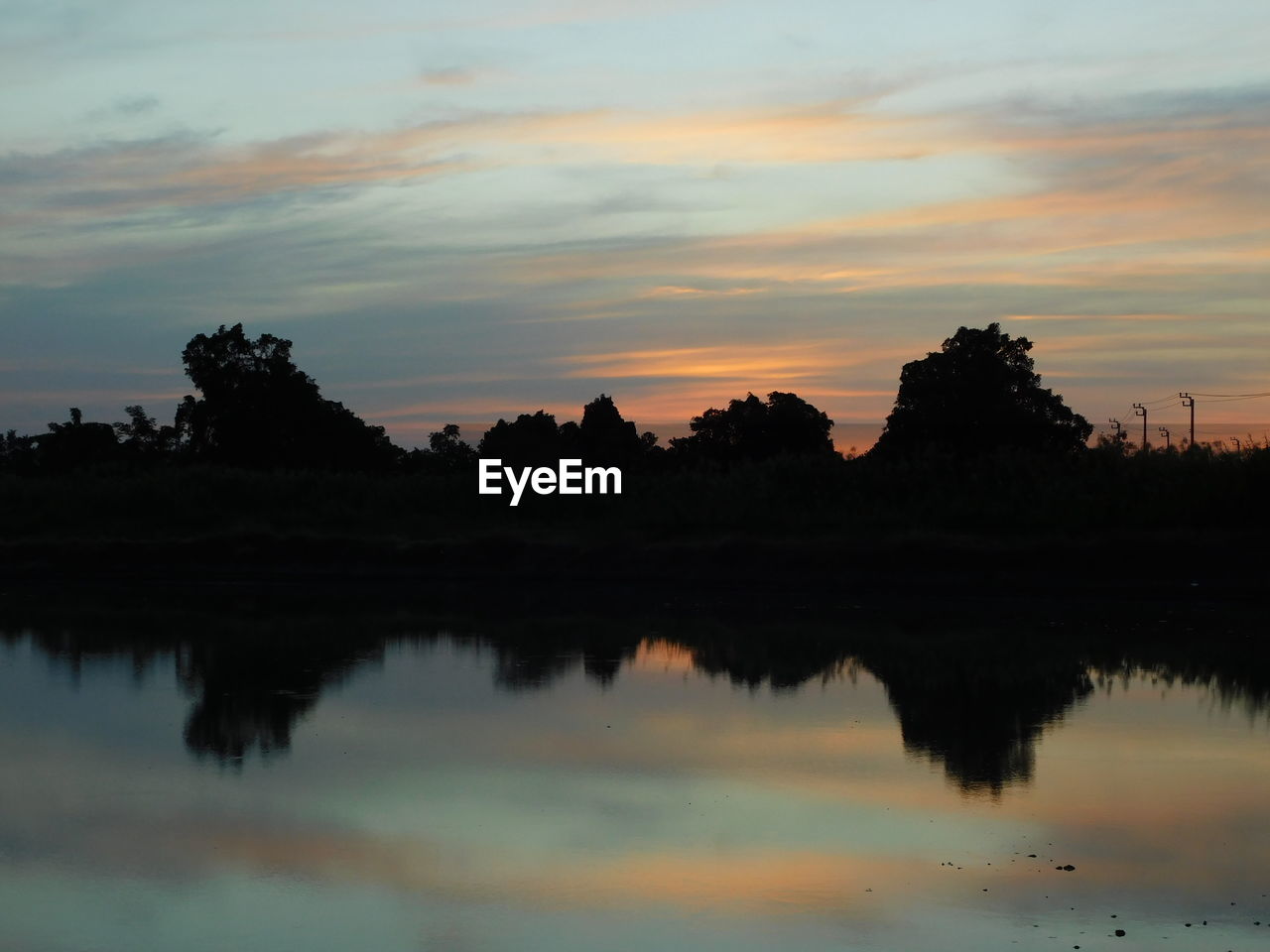 REFLECTION OF SILHOUETTE TREES ON LAKE AGAINST SKY