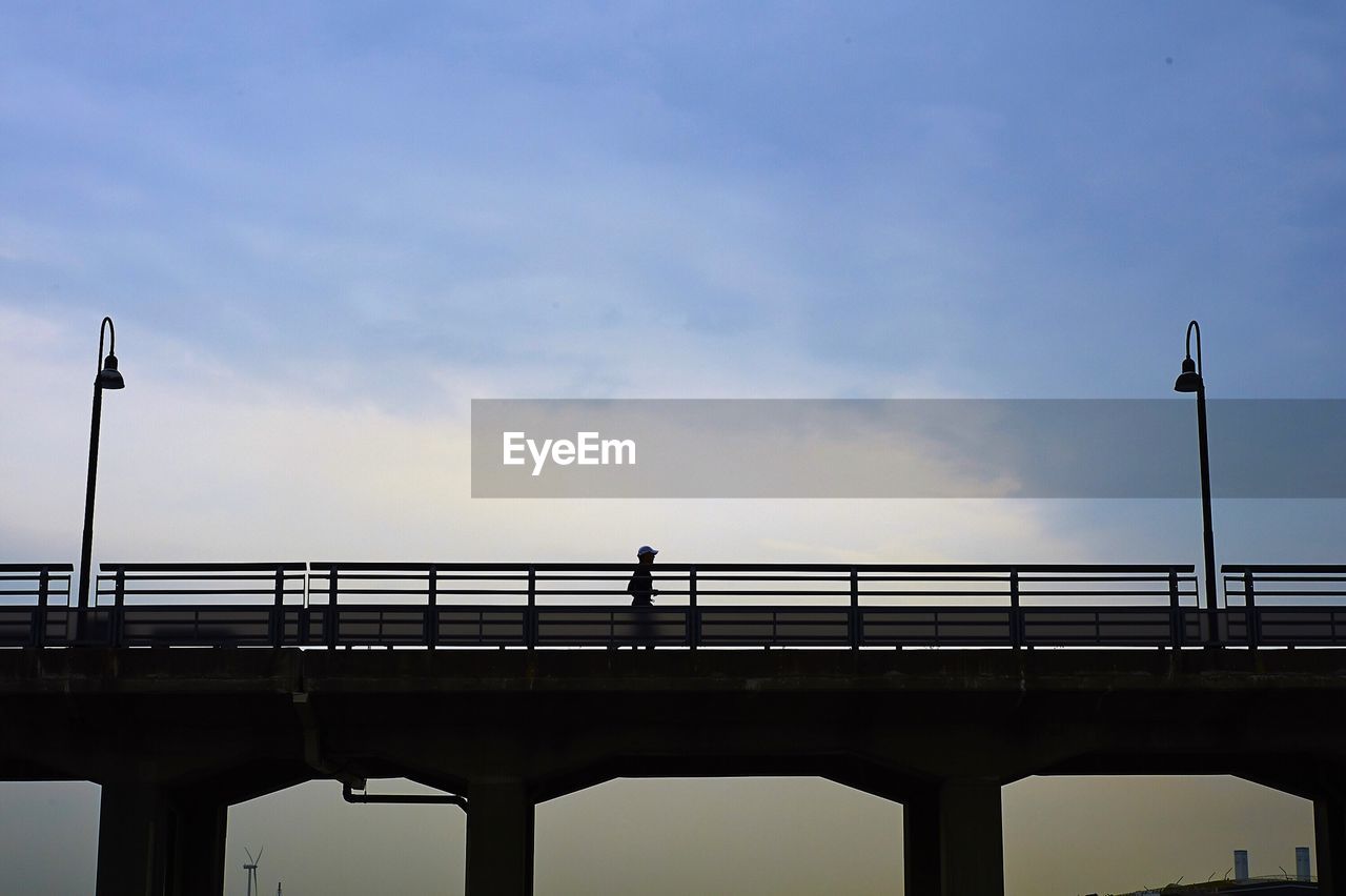 Low angle view of silhouette person walking on bridge