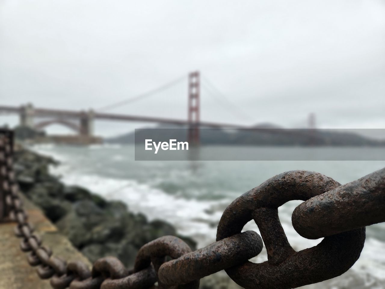 bridge, suspension bridge, water, metal, architecture, built structure, transportation, sky, nature, travel destinations, focus on foreground, no people, sea, strength, rusty, fog, chain, steel cable, day, iron, city, tourism, outdoors, travel, bay of water, bay, steel, alloy, urban skyline, cloud, land, close-up, copy space, rope