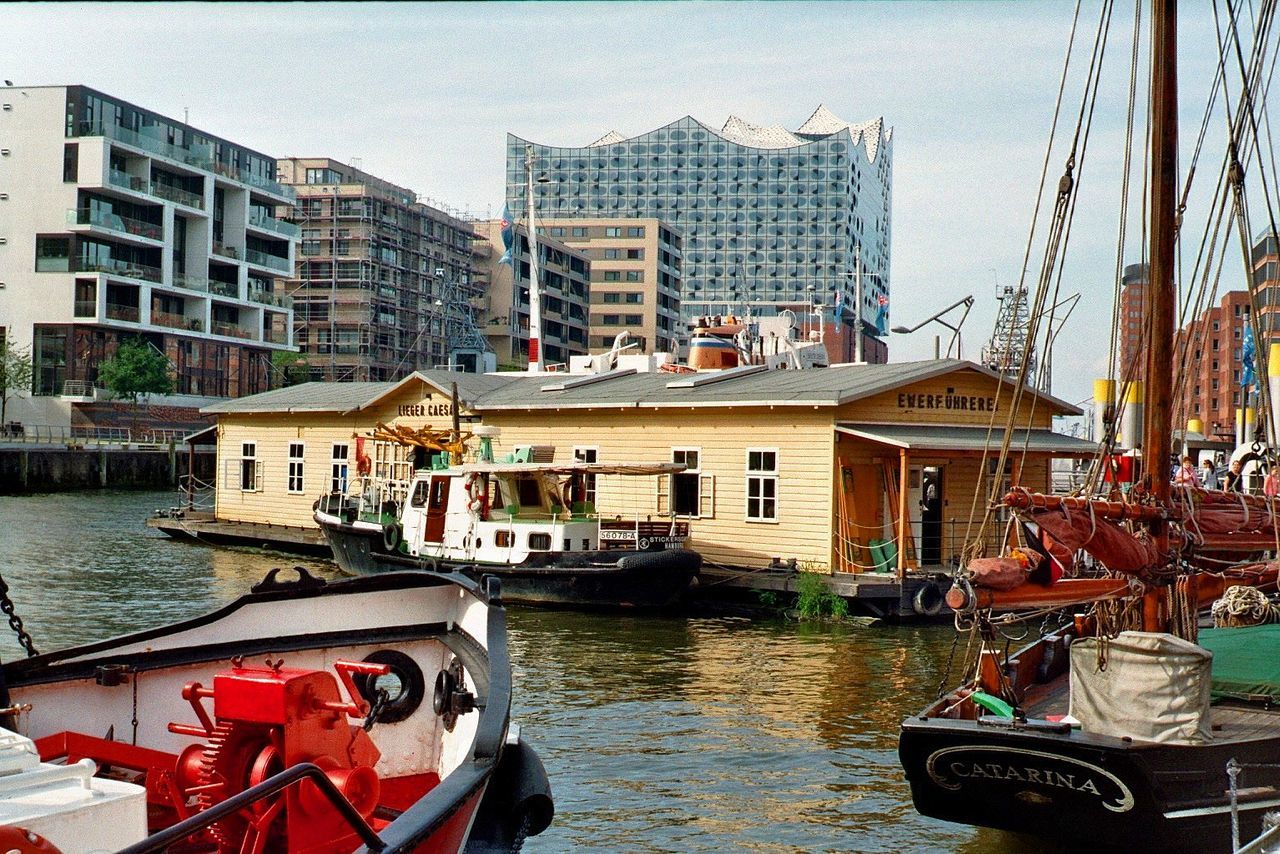 BOATS MOORED IN RIVER WITH BUILDINGS IN BACKGROUND