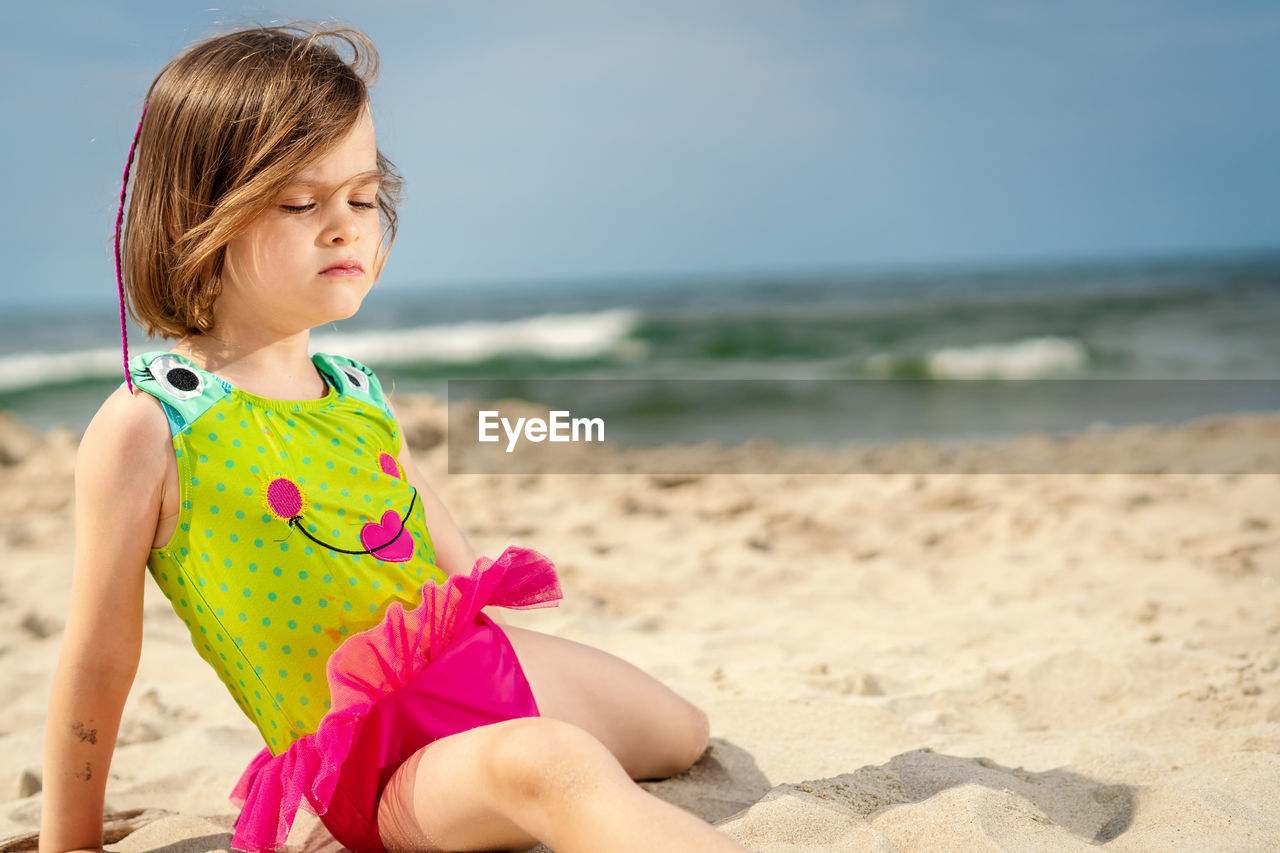 Girl relaxing on sand at beach against sky