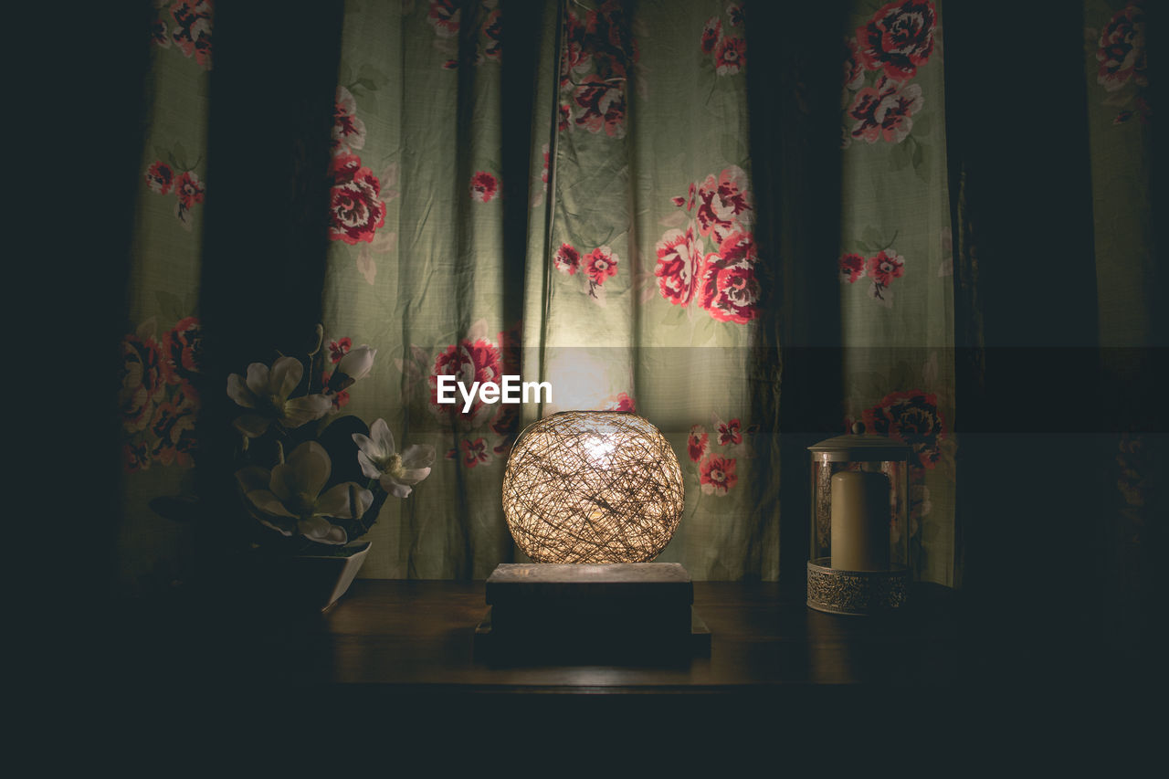 Illuminated lamp on table against curtain in darkroom