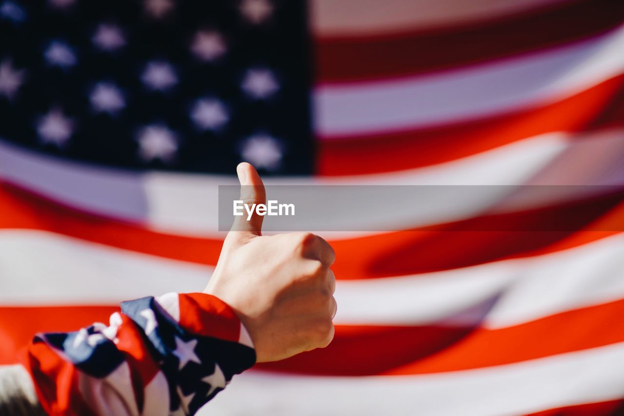 Cropped hand gesturing thumbs up sign against american flag