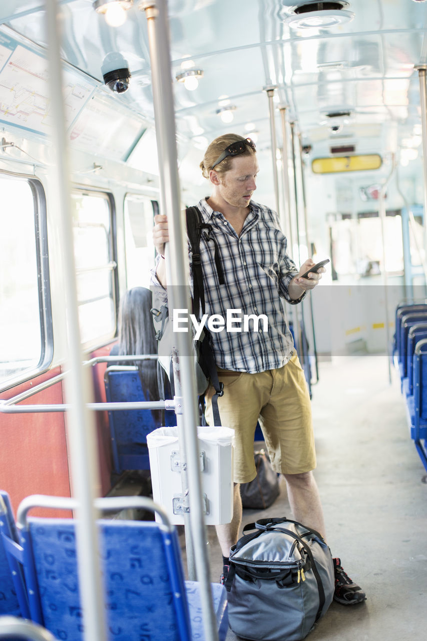 Man using mobile phone while standing by luggage in metro train