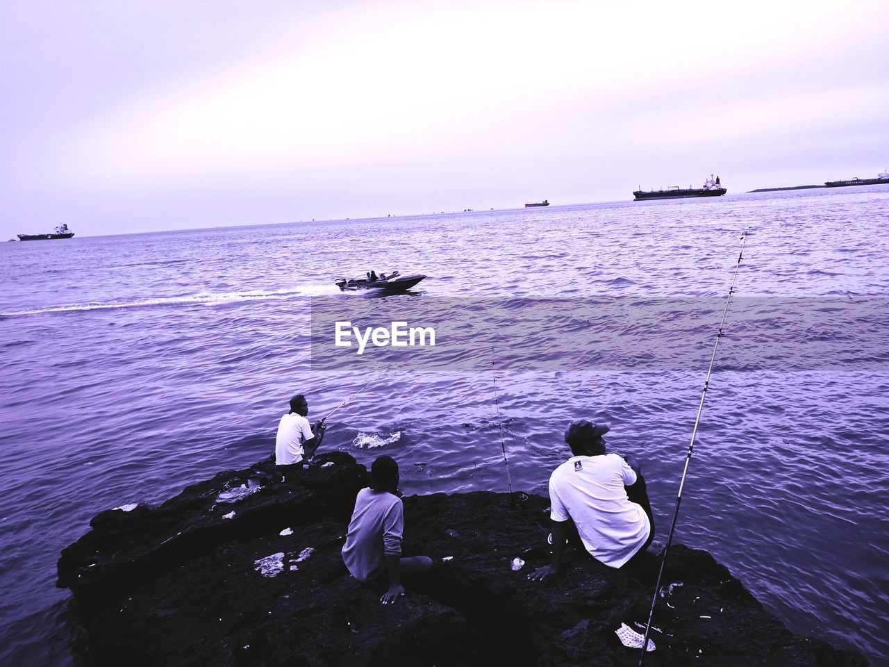 PEOPLE FISHING AT SEA AGAINST SKY