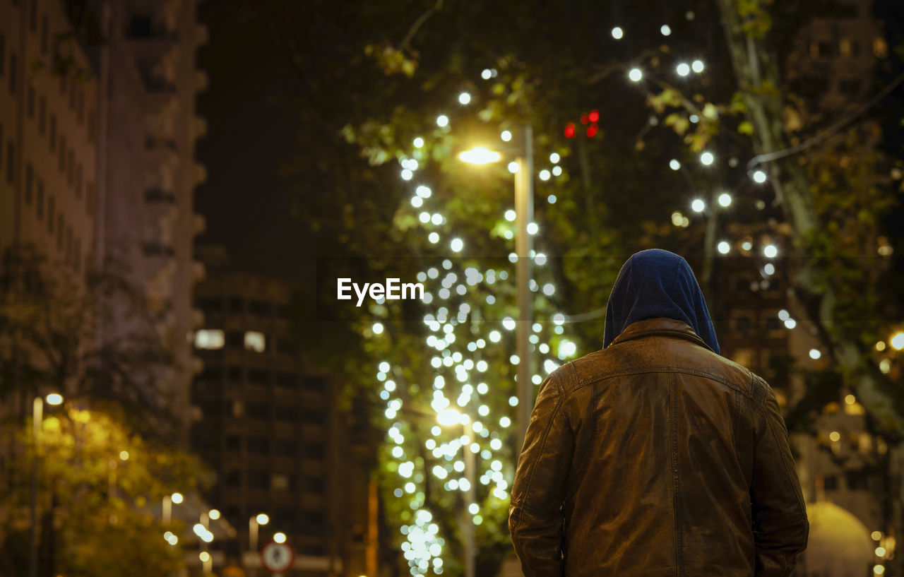 Rear view of adult man on street at night with lights of christmas