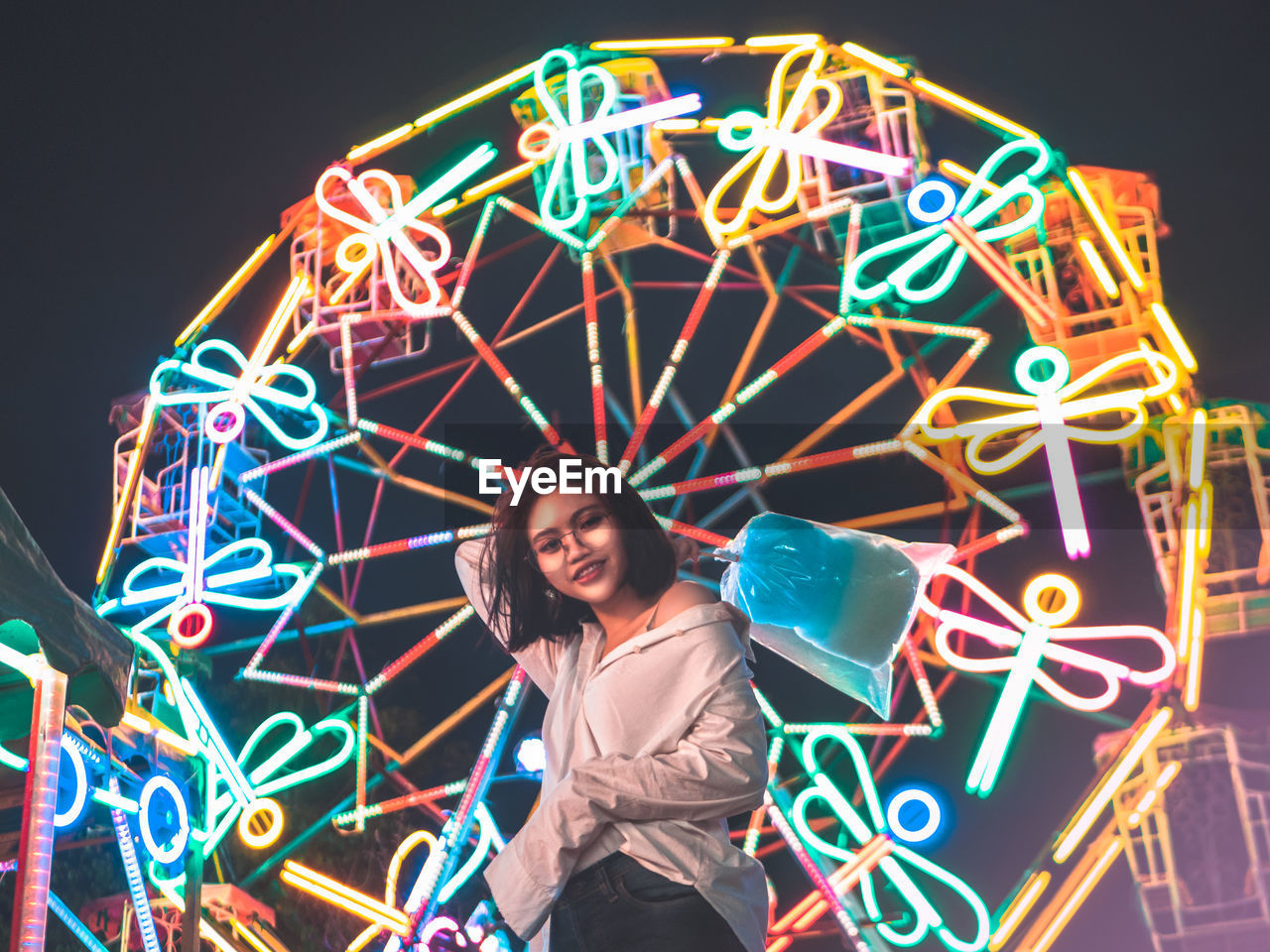 Portrait of woman against illuminated ferris wheel in amusement park at night