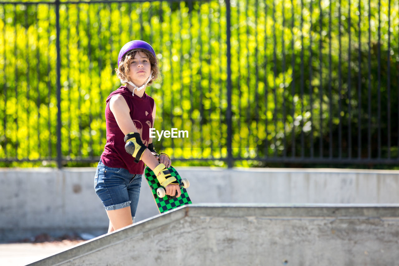 Skater girl holds her skateboard while looking toward the camera