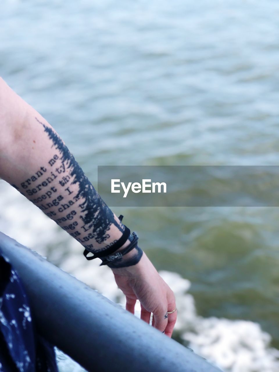 Cropped image of woman with tattooed hand against sea