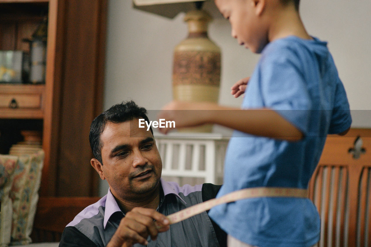 Tailor measuring waist of boy at home