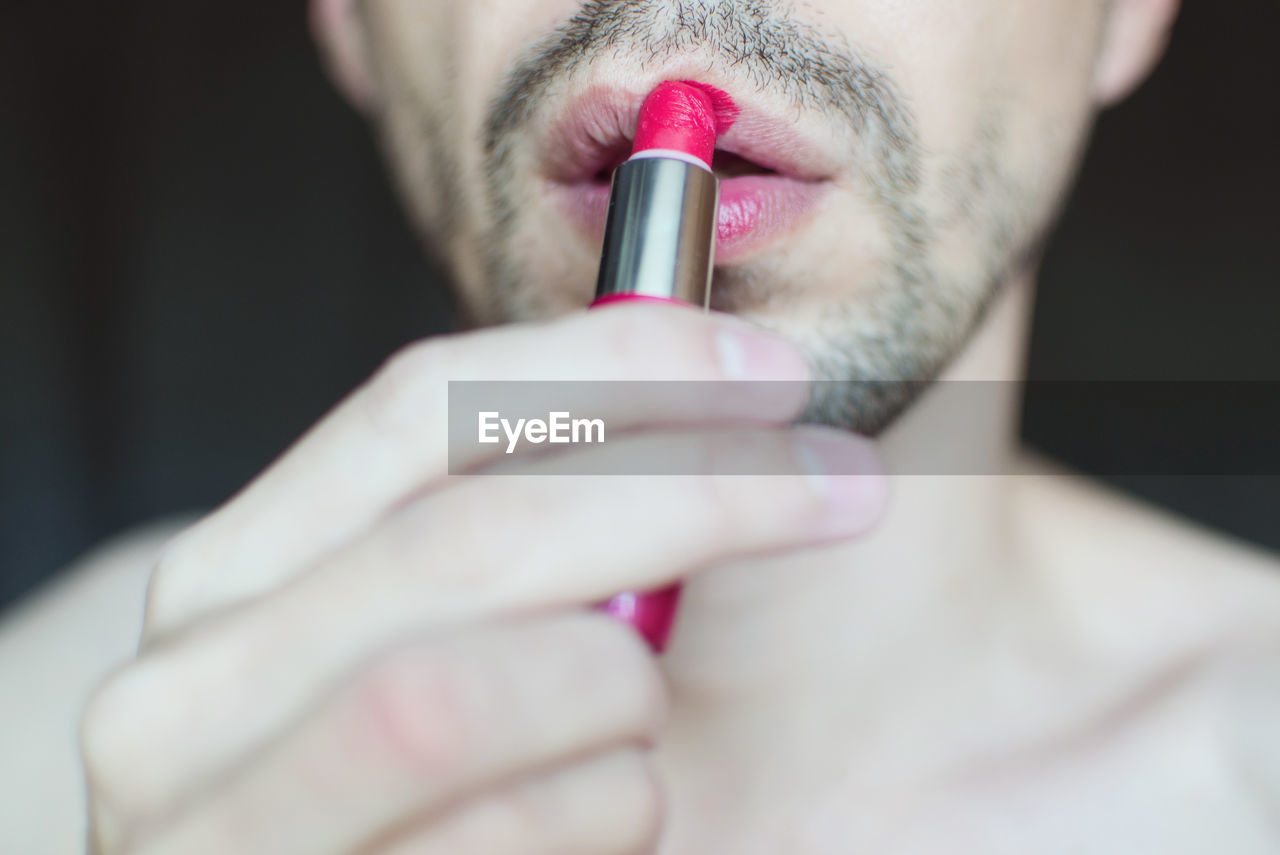 Midsection of transgender man applying red lipstick