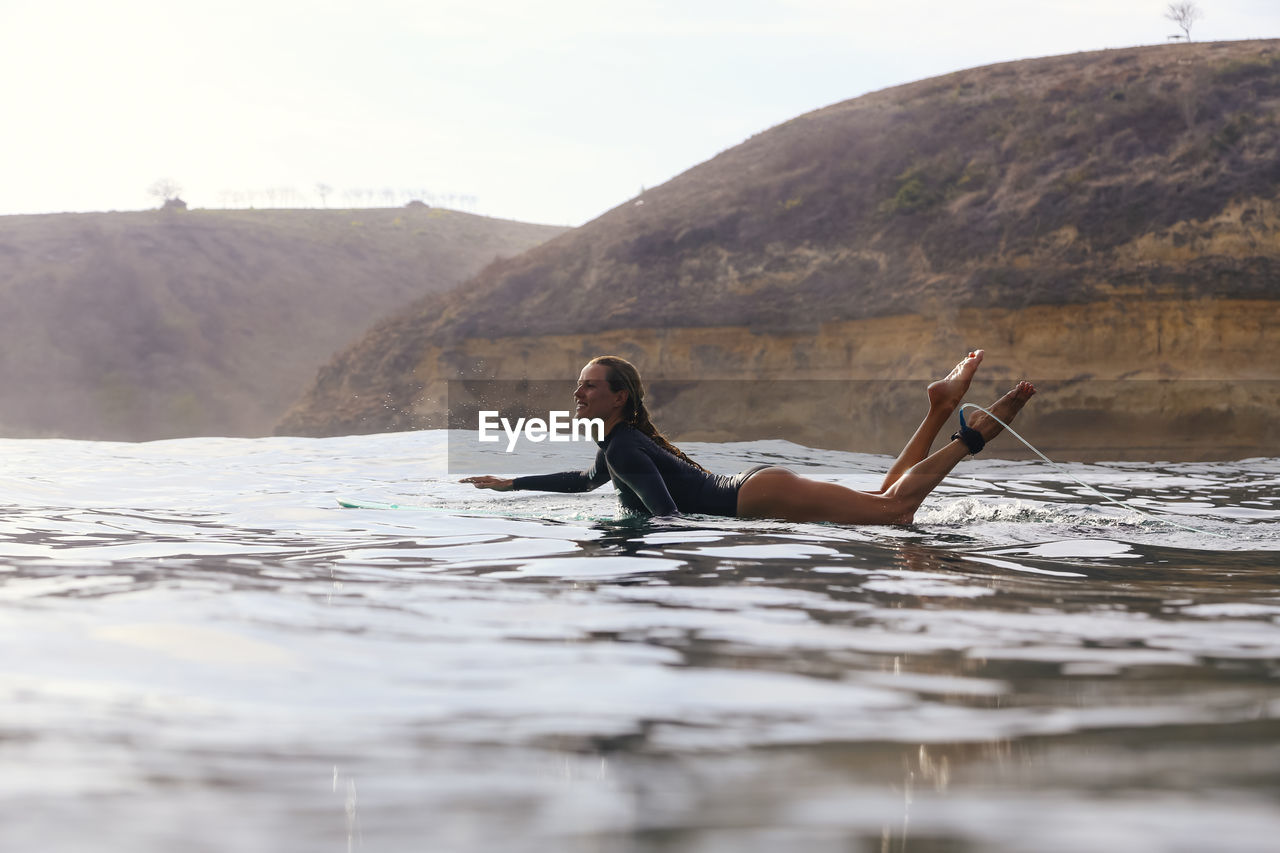 Happy woman sitting on surfboard in sea