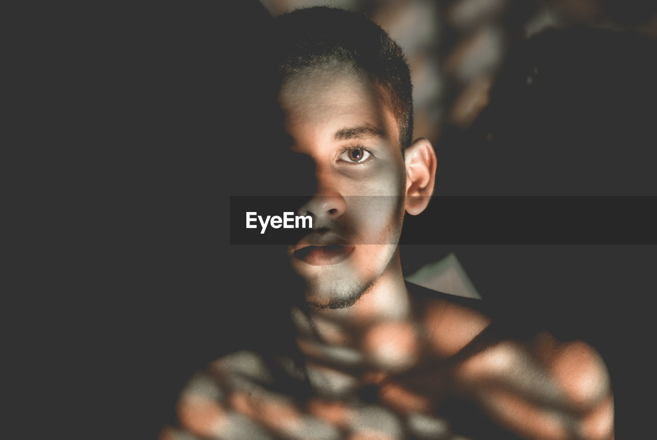 Close-up portrait of young man with shadow on body in darkroom