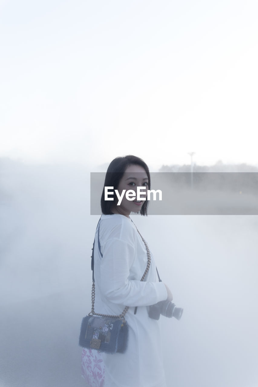 Young woman standing amidst fog against sky