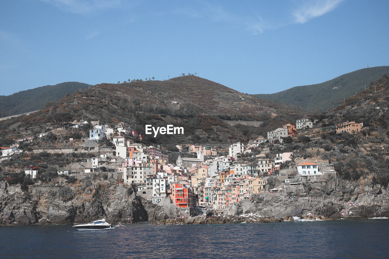 Aerial view of buildings in town by sea against sky