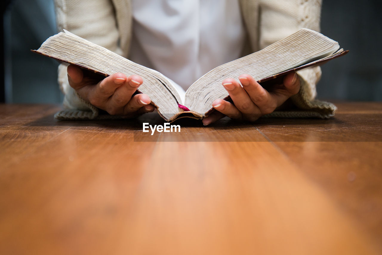 Midsection of woman reading book at table