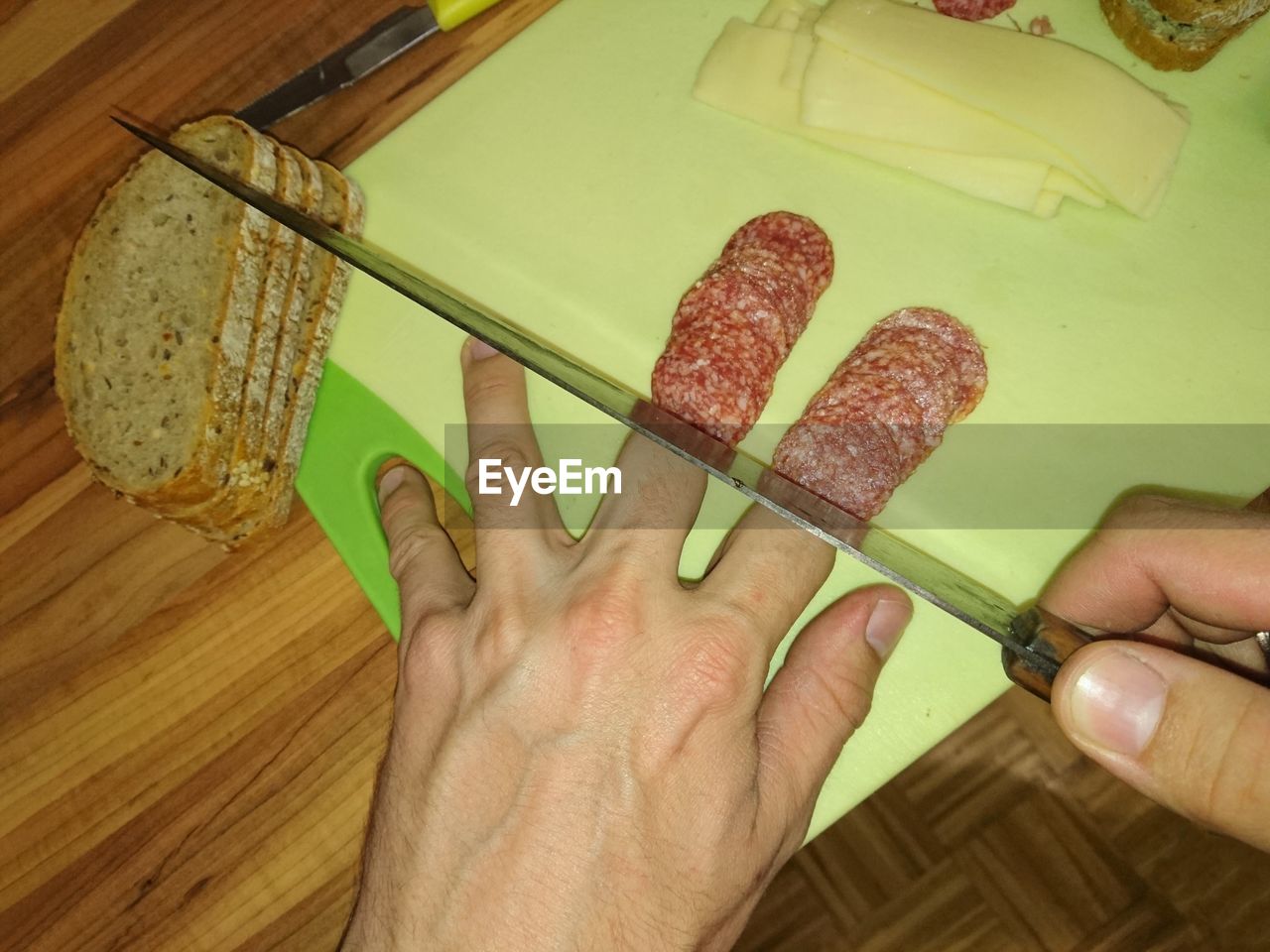 Optical illusion of cropped hand chopping sausage fingers on cutting board