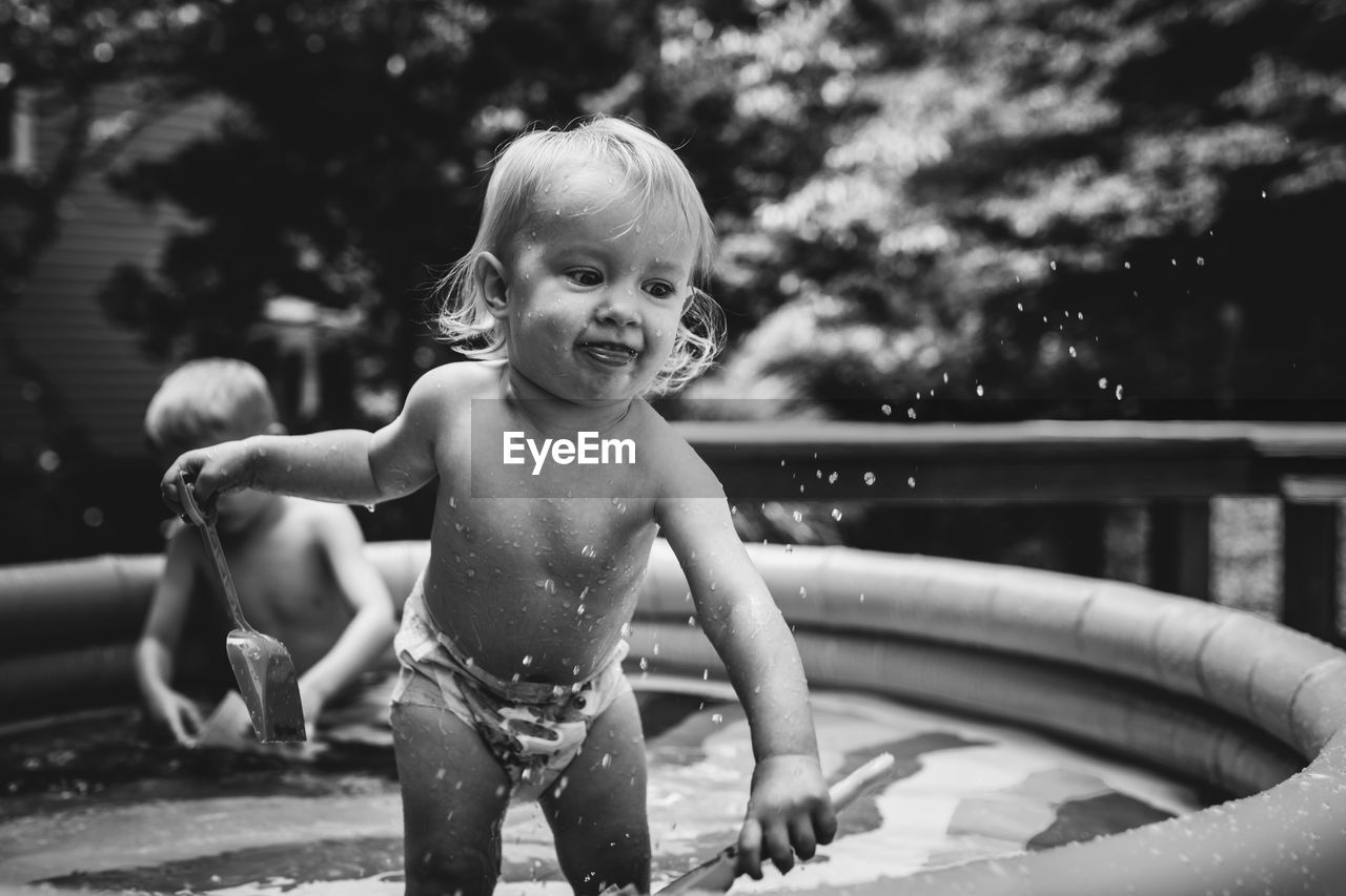 Shirtless baby girl playing in wading pool at yard