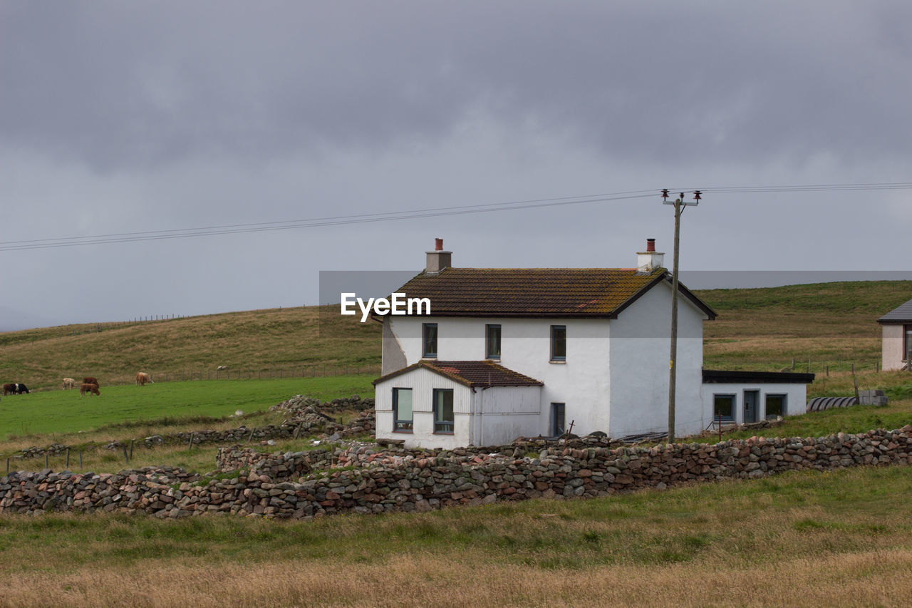 HOUSES ON FIELD BY HOUSE AGAINST SKY