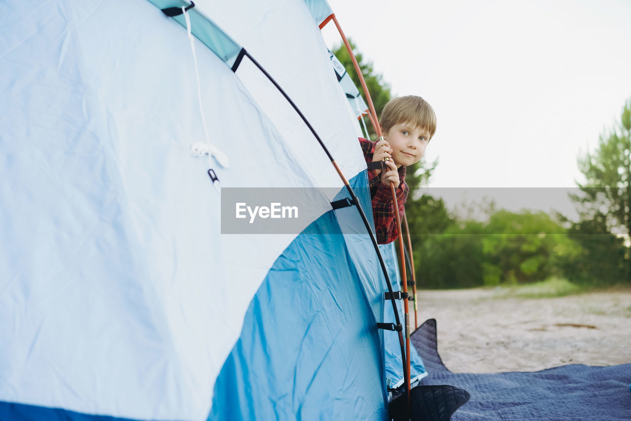 Cute little caucasian boy looking out from touristic tent. family camping concept