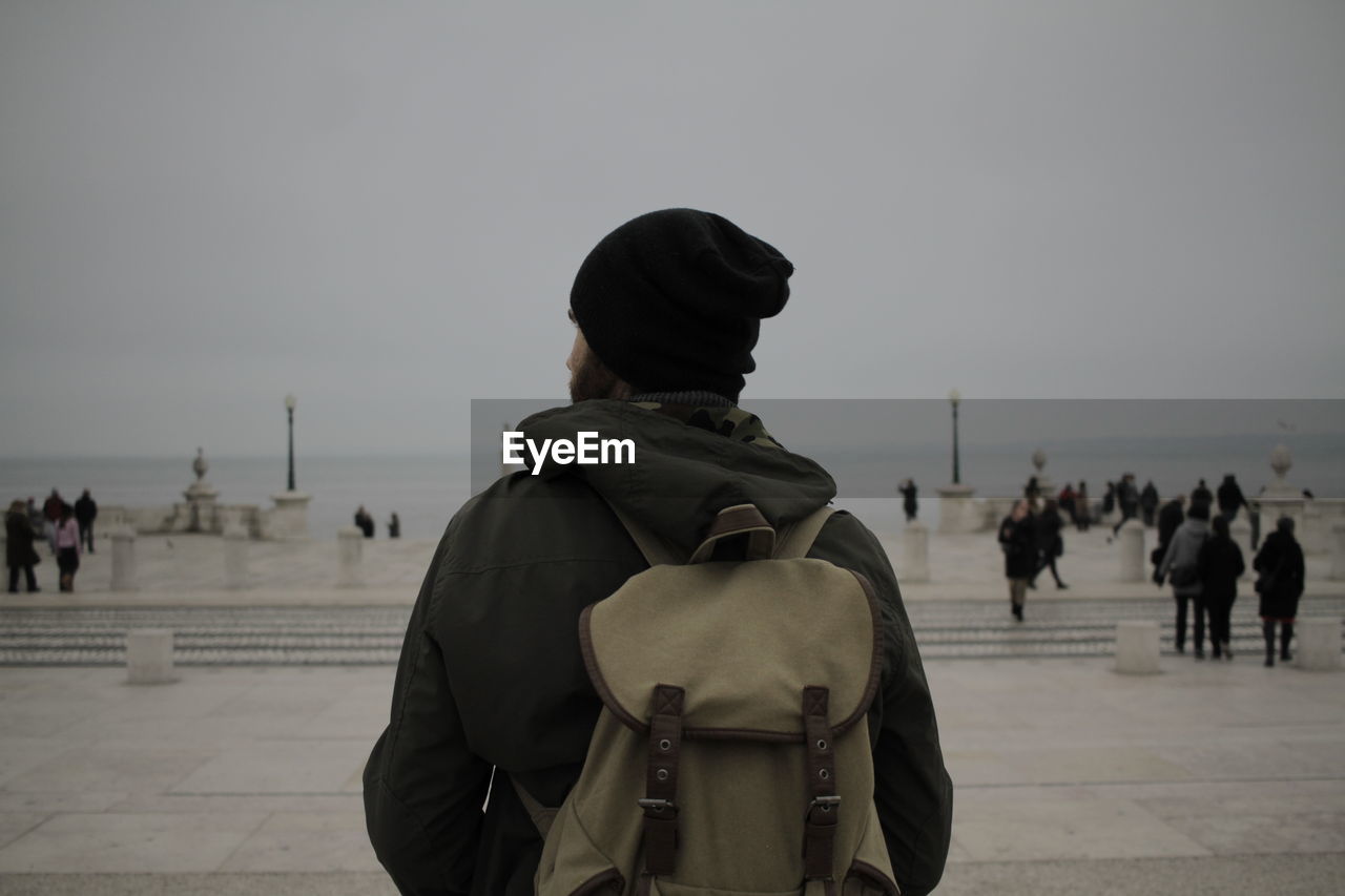 Rear view of man wearing backpack while standing at beach against clear sky