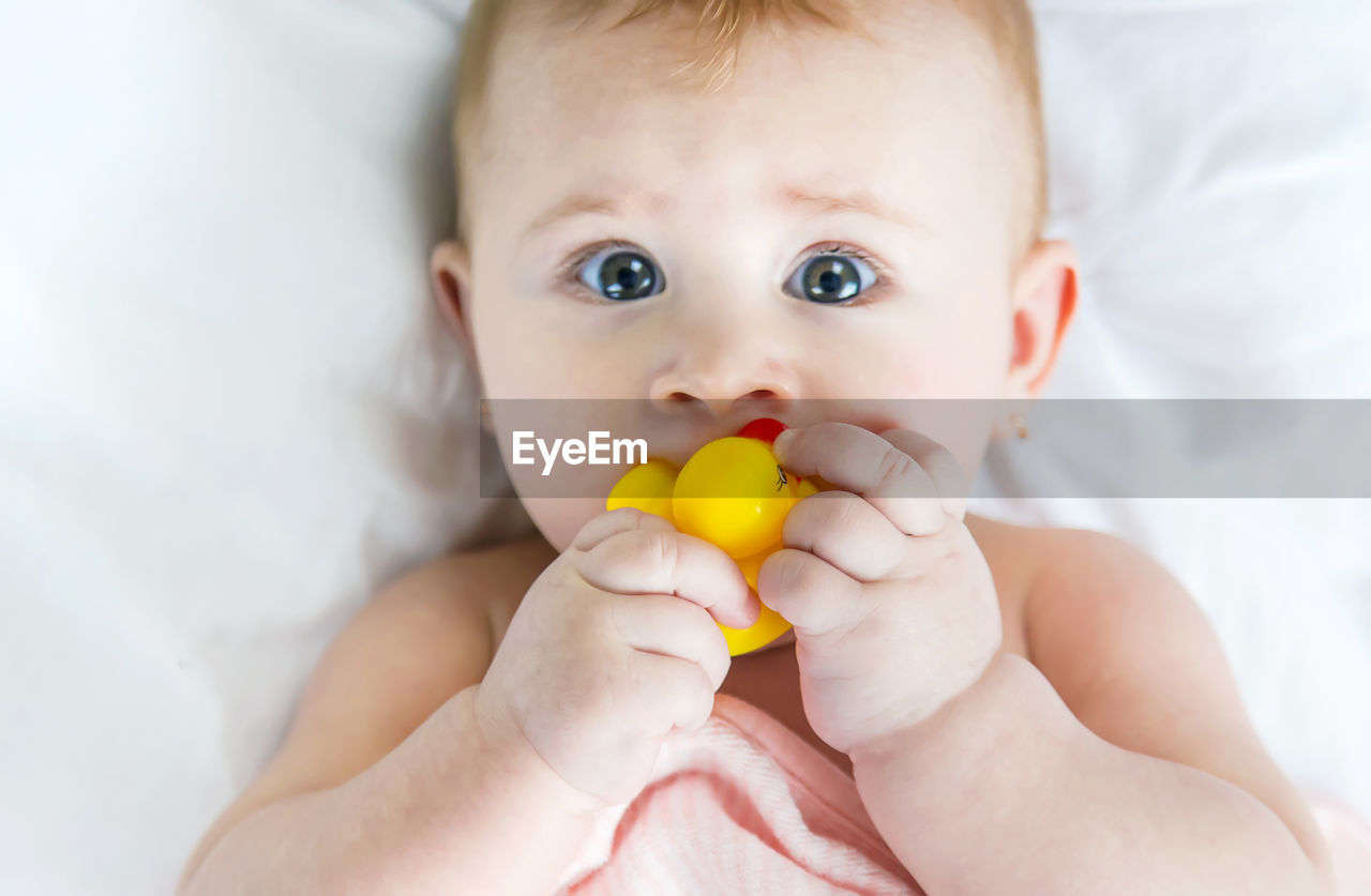 Close-up of cute baby girl holding toy lying on bed at home