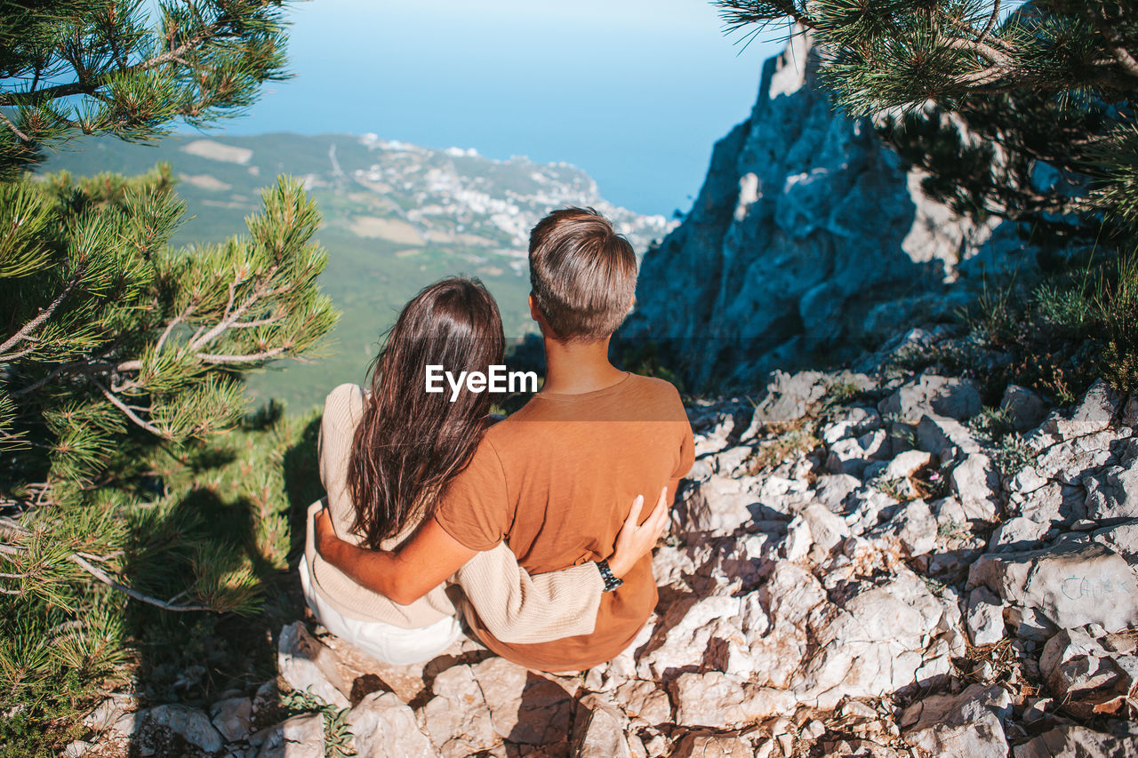 REAR VIEW OF COUPLE SITTING ON ROCK LOOKING AT VIEW OF ROCKS
